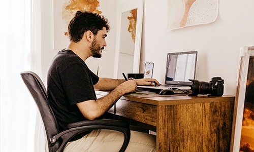 man sits at his desk with open laptop
